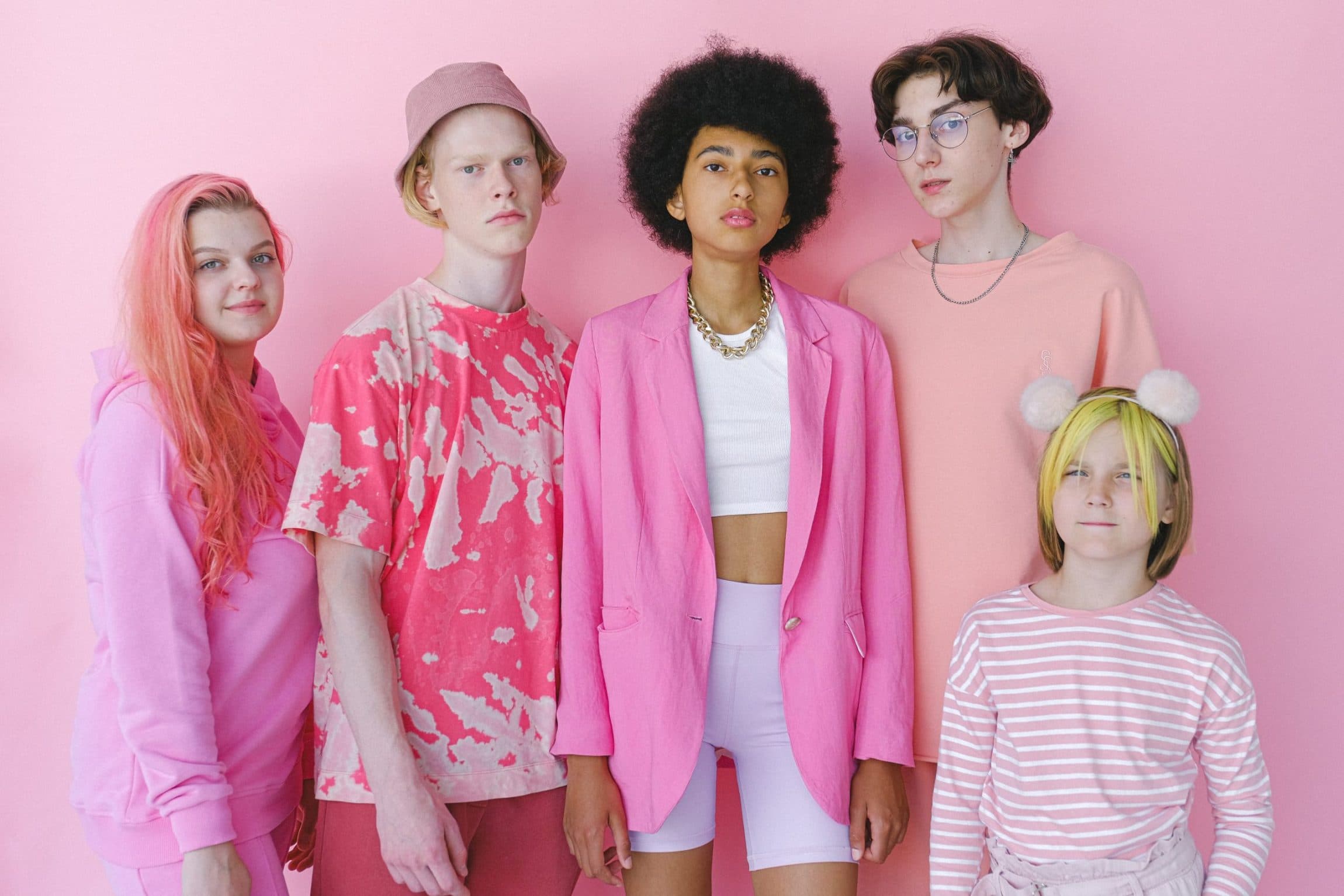 image of five young poeple all dressed various different shades of pink, all five are standing against a pink background.