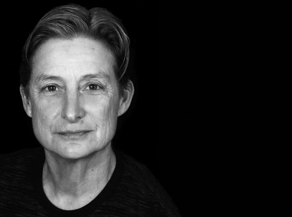 Judith Butler photographed against black backrgound. Photo is in black and white showing only their face and neck