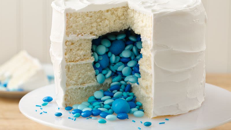 close up of a white vanilla layered cake which has been cut open to reveal blue lollies on the inside of a gender reveal cake.