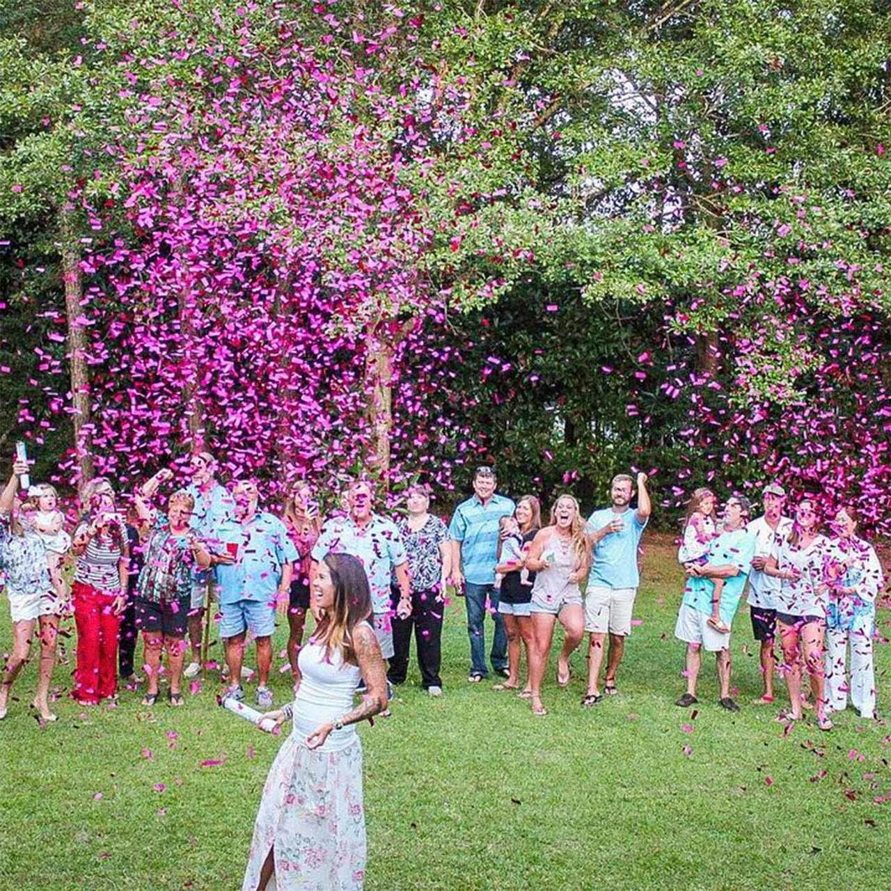 large family celelbrating gender reveal. pink coloured confetti fired by mum to be in foreground.